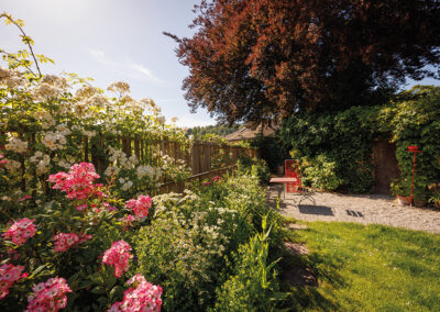 Der neue Zaun auf der Grundstücksgrenze schafft Struktur und schliesst den Garten räumlich ab. Inmitten von Rosen lädt ein Kiesplatz zum Verweilen.